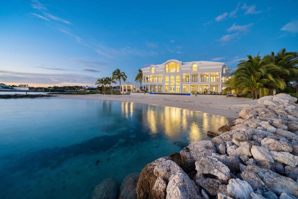 Elegant beachfront villa with palm trees and clear water at sunset.