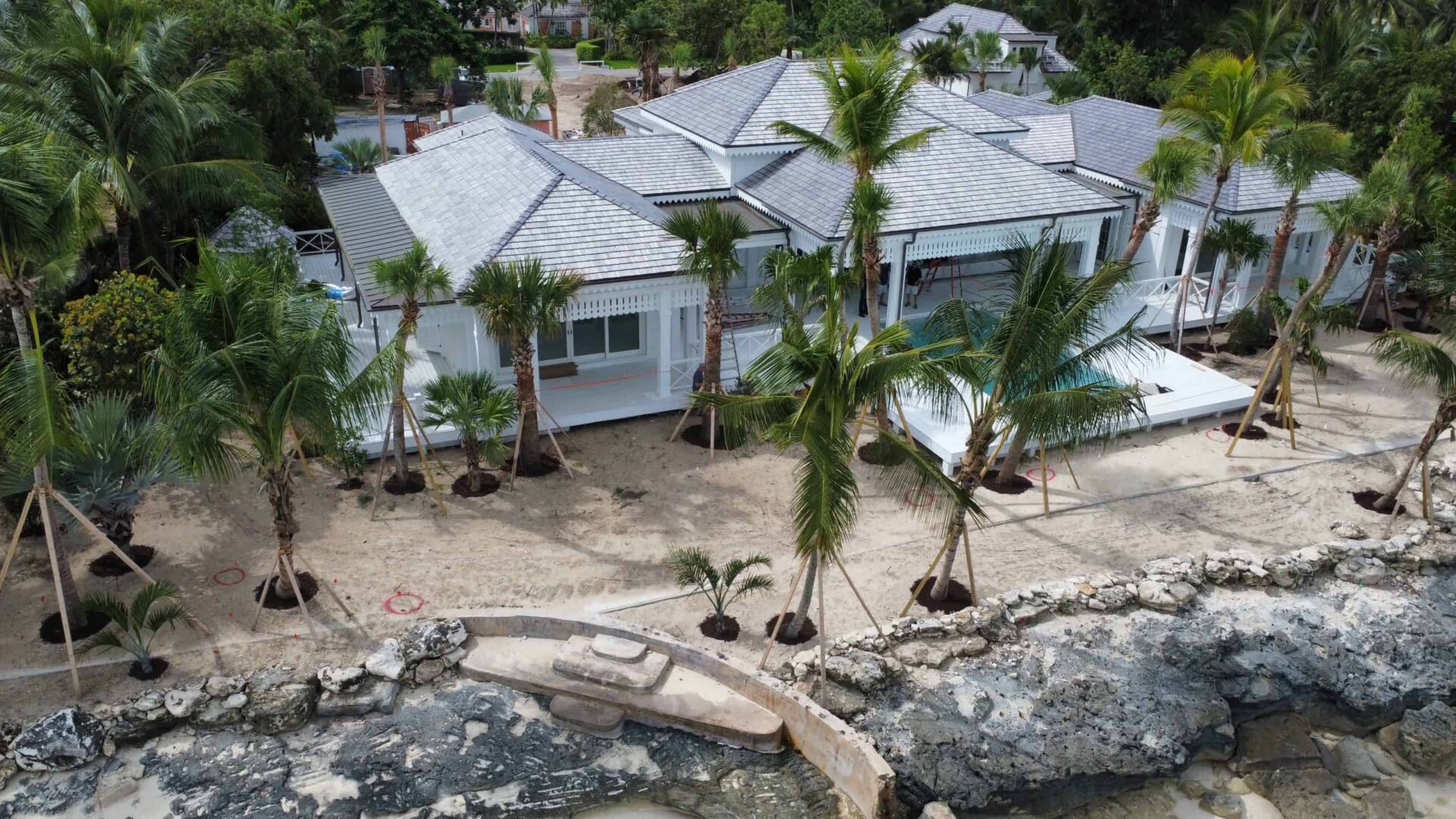 Elegant beachfront villa with palm trees and rocky shoreline in Bahamas.