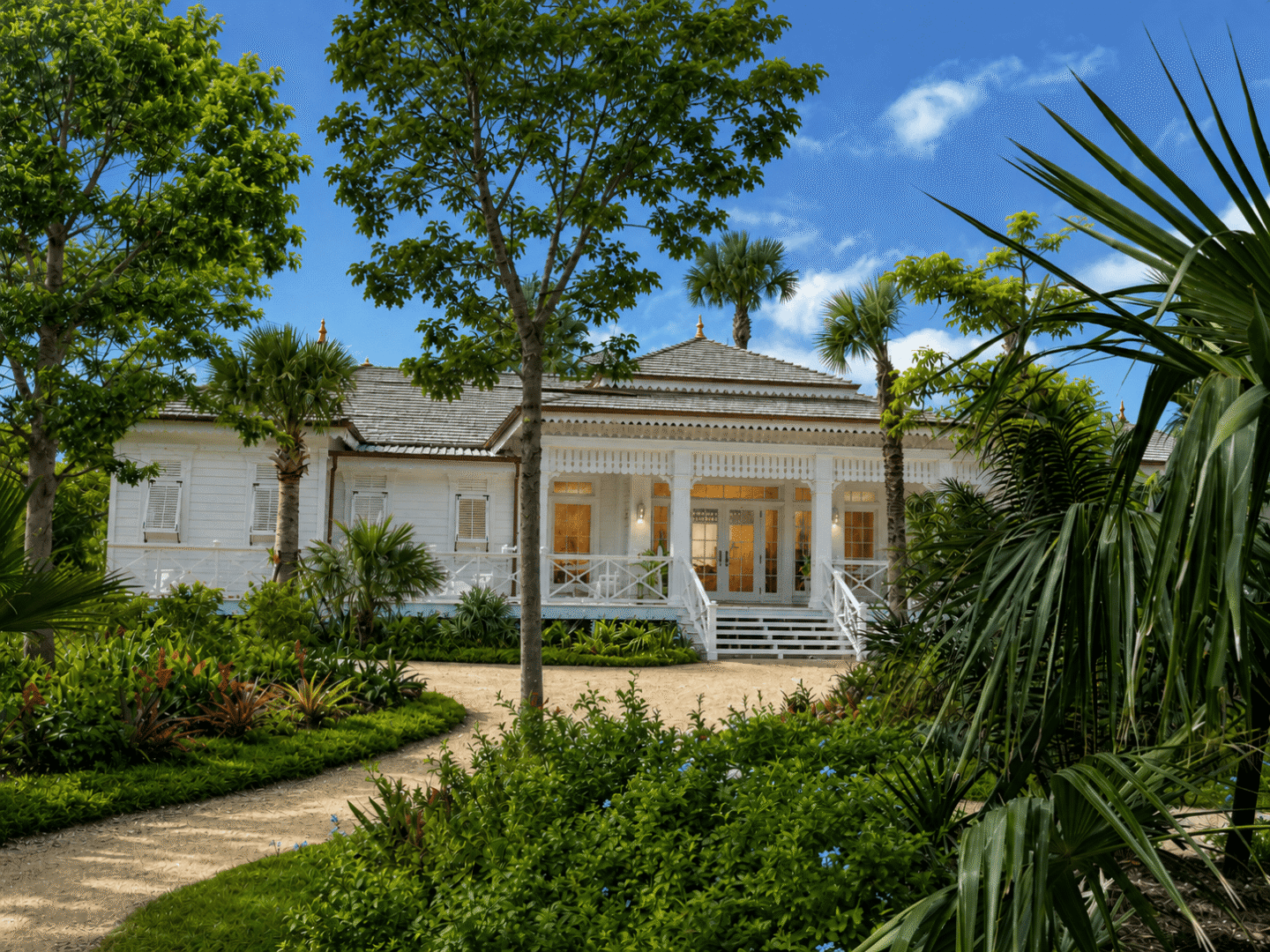 Beautiful Bahamian villa surrounded by lush tropical gardens and palm trees under a blue sky.