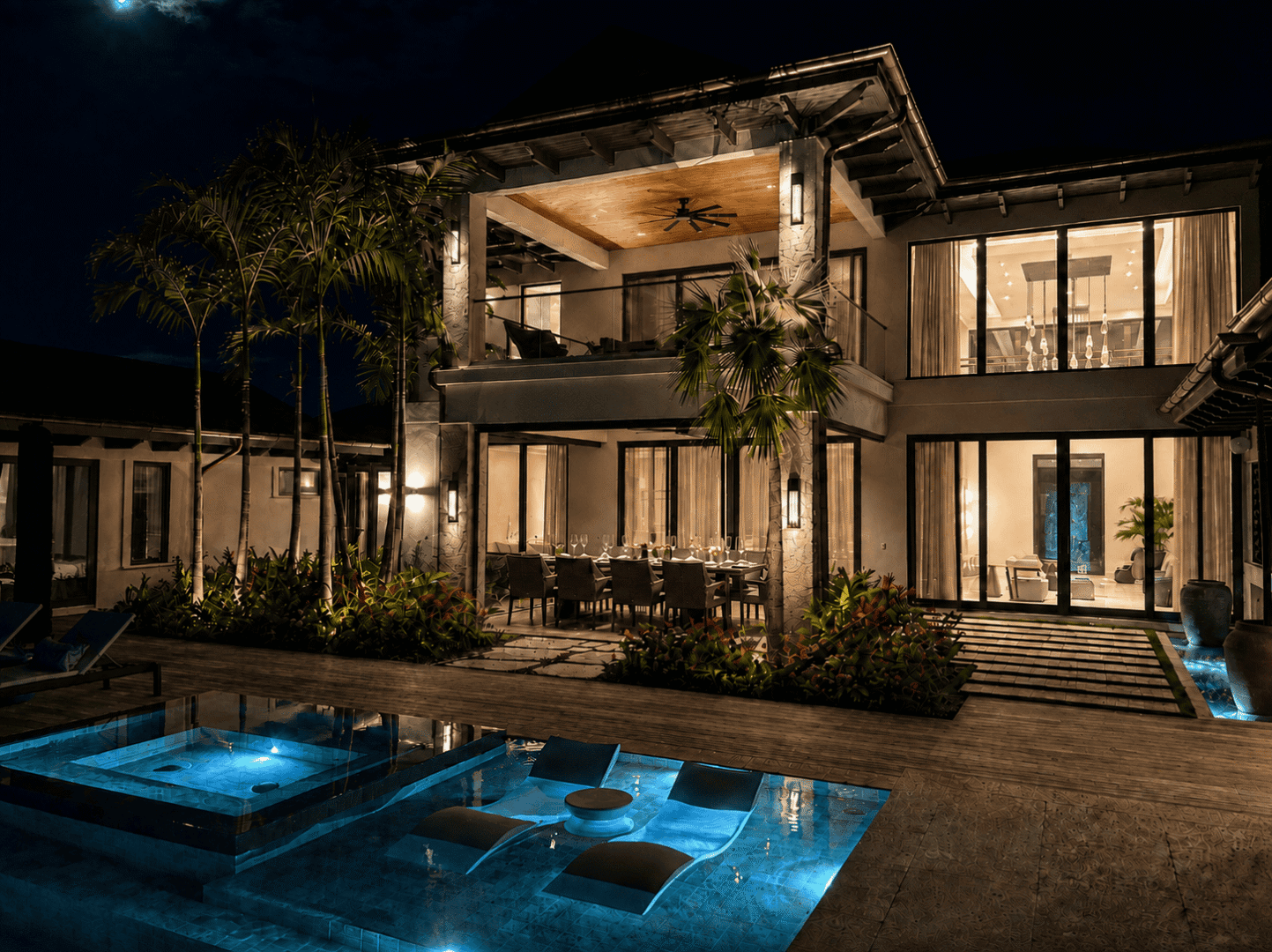 Night view of a luxury Bahamas villa with illuminated pool and outdoor dining area.
