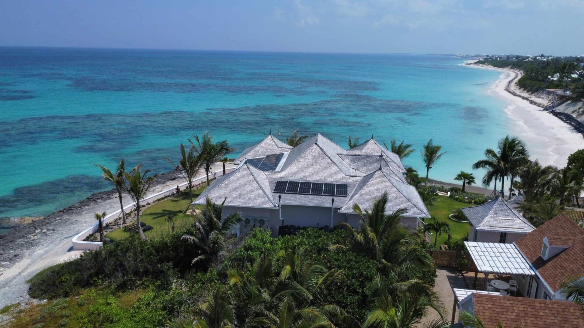 Luxury private residence on Hope Town's beachfront with palm trees and turquoise waters.