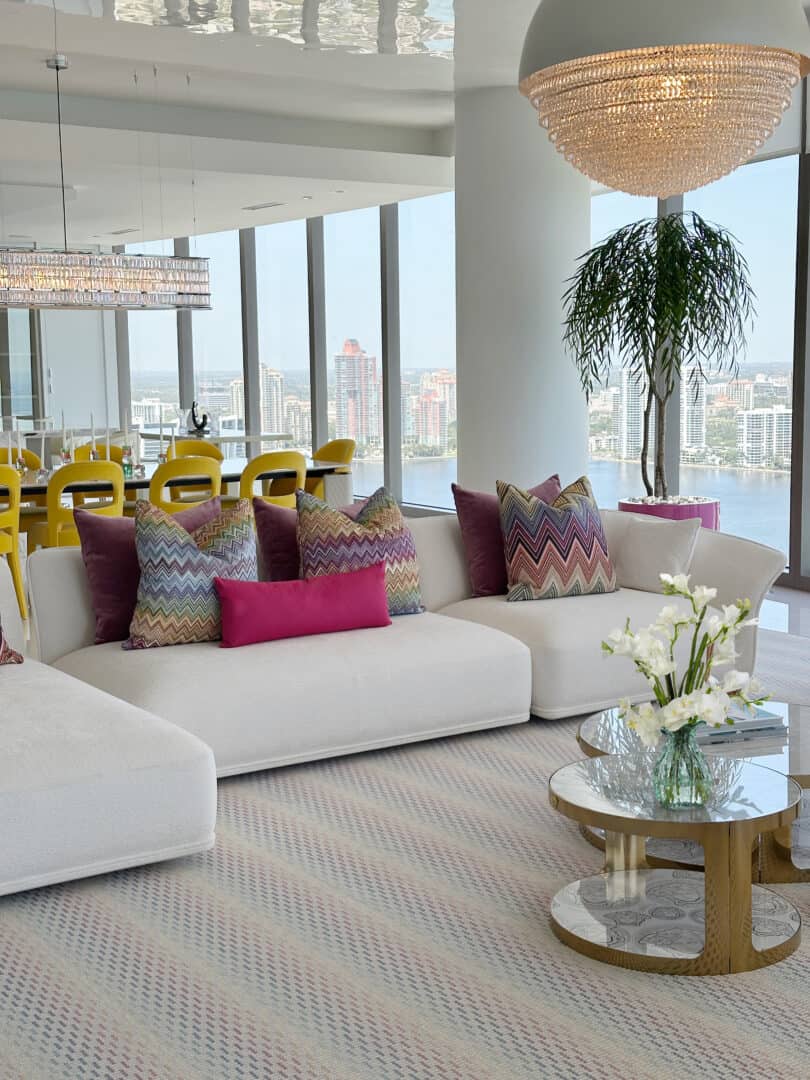Luxurious modern living room with city view, white sofa, colorful pillows, and chandelier.