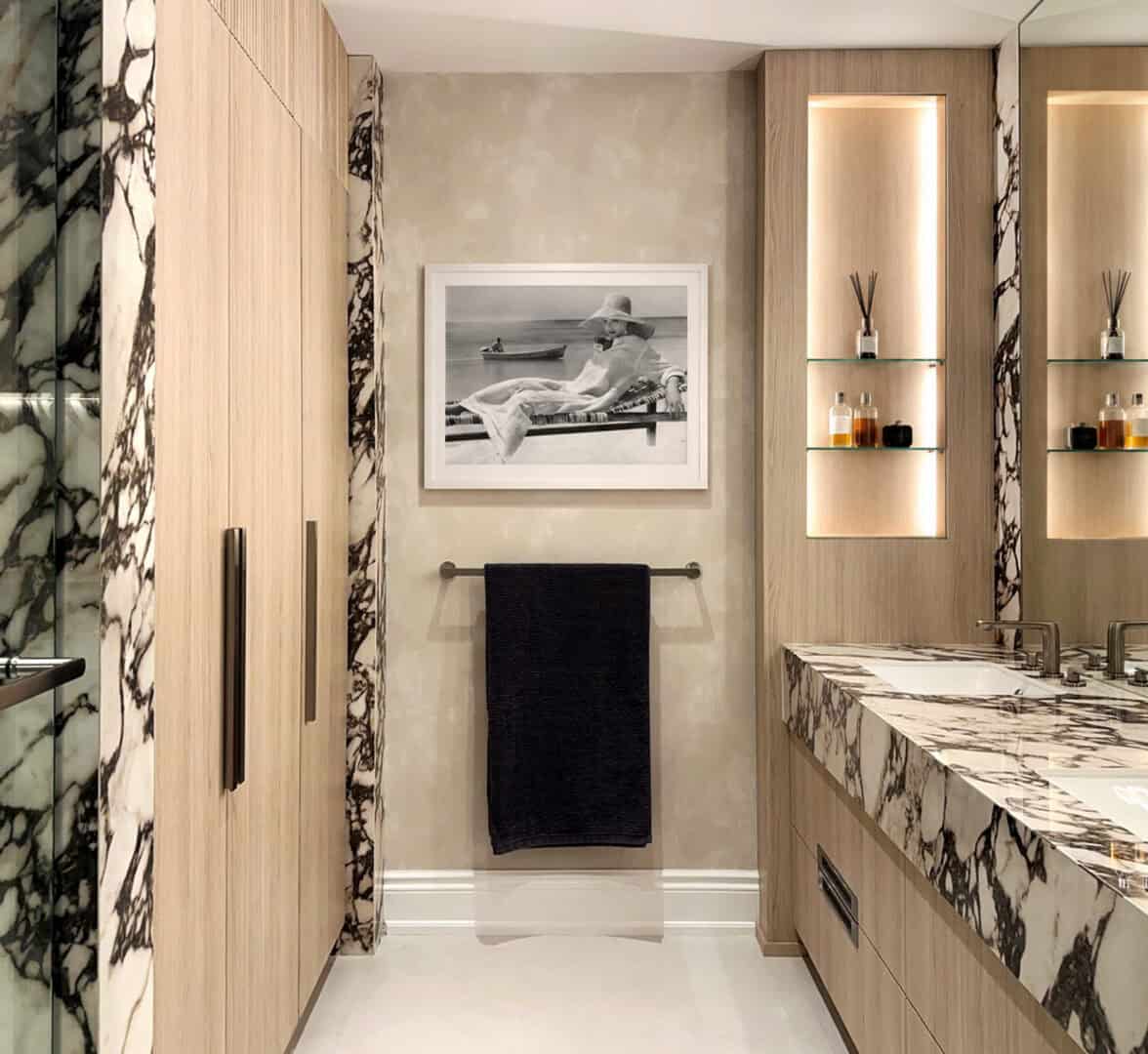 Modern bathroom with marble accents, wooden cabinets, and black towel.