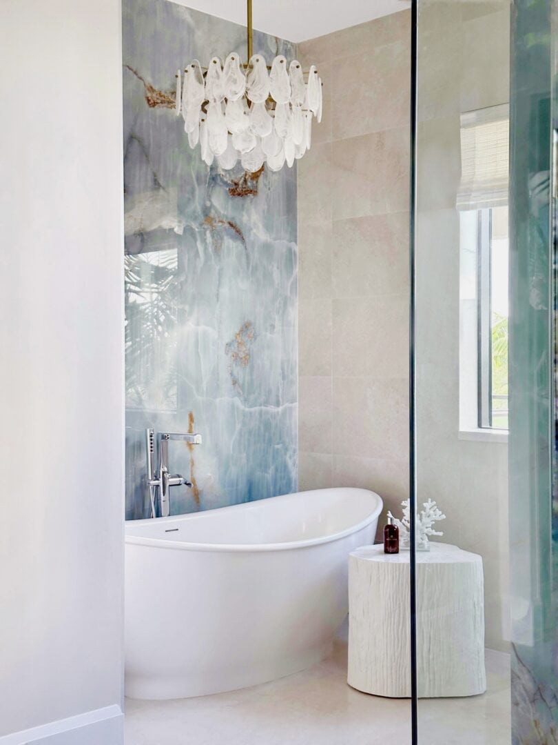 Modern bathroom with freestanding bathtub, chandelier, and marble wall.