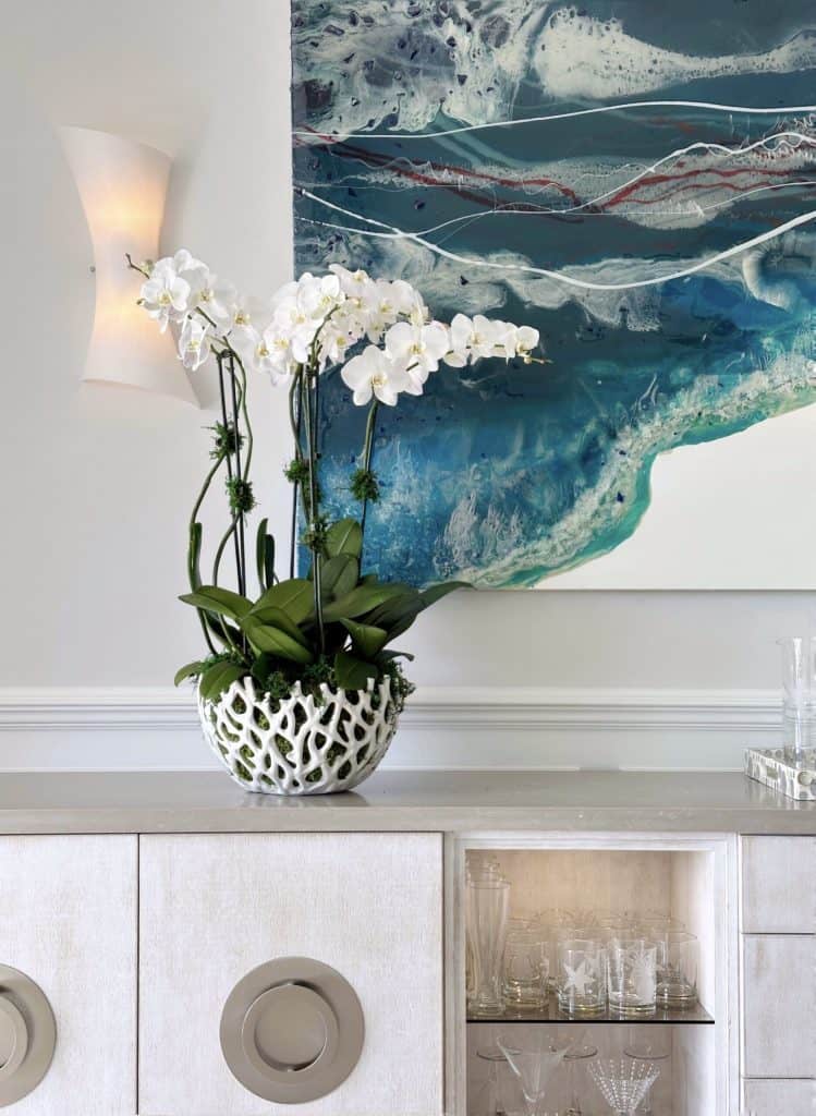 Elegant white orchid plant on a modern white cabinet with abstract wall art.